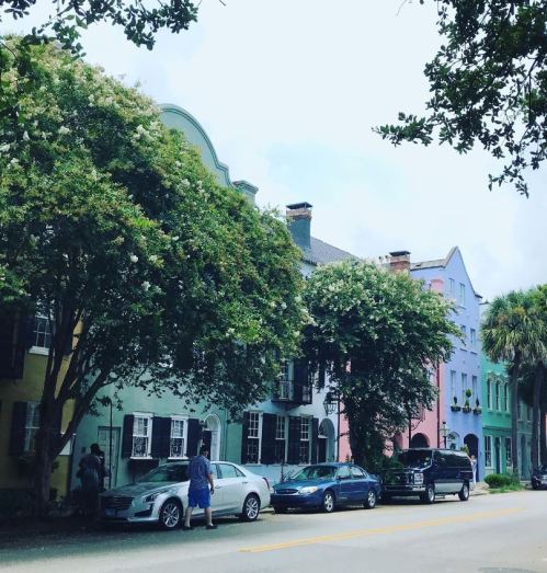 Colorful historic buildings lined with trees and parked cars on a sunny street.