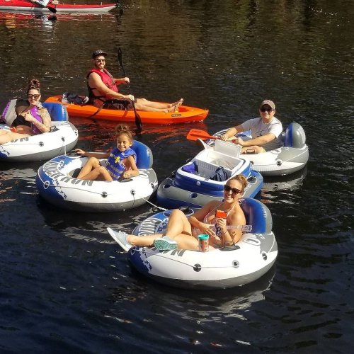 A group of people relaxing on inflatable tubes and a kayak in a calm water setting, enjoying a sunny day.