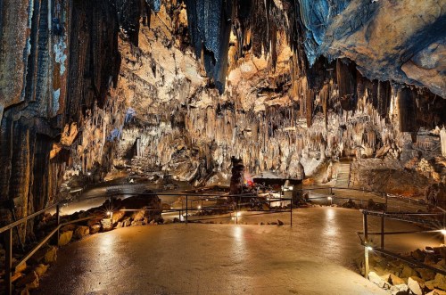 A vast cave interior with stalactites and stalagmites, illuminated pathways, and a natural rock formation.