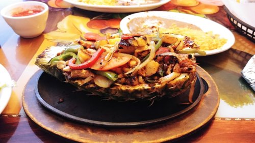 A grilled pineapple filled with sautéed vegetables and meat, served on a wooden platter with colorful table decor.