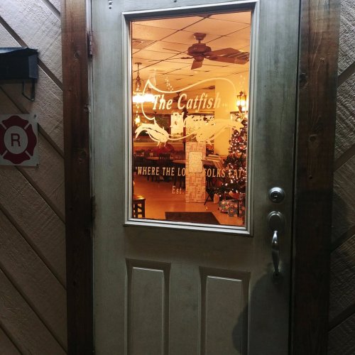 A wooden door with a glass window displaying "The Catfish" and a cozy restaurant interior visible through the glass.