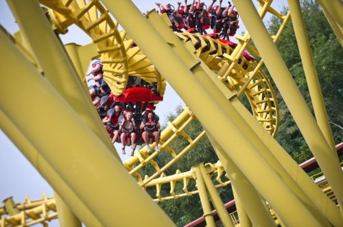 A roller coaster with riders enjoying a thrilling loop, surrounded by yellow tracks and greenery in the background.