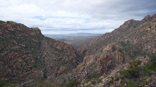 A panoramic view of rocky mountains and valleys under a cloudy sky, with distant hills visible in the background.