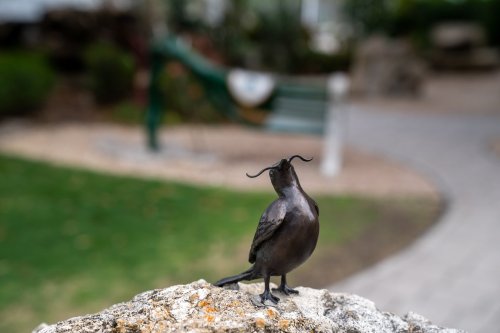 A bronze bird sculpture perched on a rock, with a blurred garden and hammock in the background.