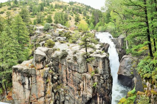 A scenic view of a waterfall cascading over rocky cliffs, surrounded by lush greenery and trees.