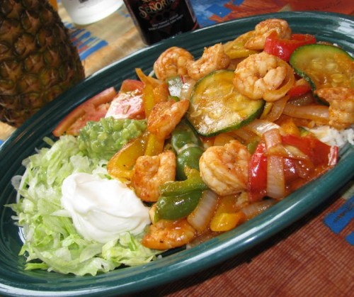 A vibrant plate of shrimp stir-fry with bell peppers, onions, and zucchini, served with lettuce and sour cream.