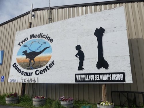 Sign for Two Medicine Dinosaur Center featuring a dinosaur silhouette, a child, and a large bone graphic.