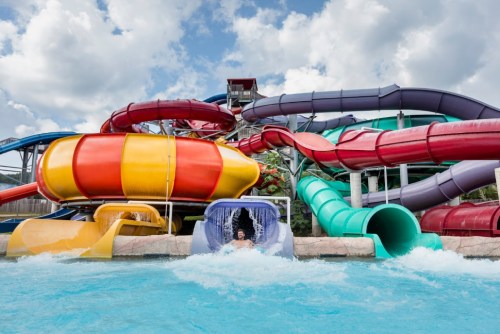 A colorful water slide complex with multiple slides and a pool, featuring a person splashing into the water below.