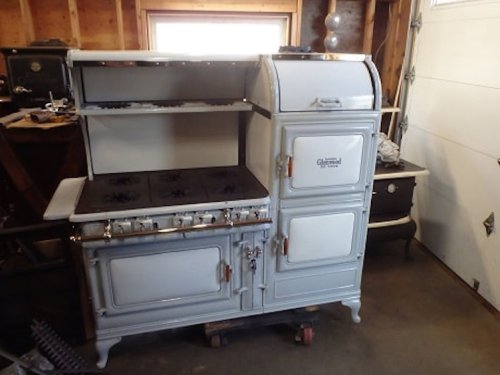 Vintage white and gray kitchen stove with four burners and an oven, set in a garage with wooden walls.