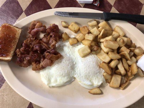 A plate of breakfast featuring two fried eggs, crispy bacon, diced potatoes, and a slice of toast.