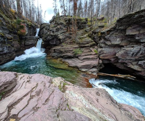 A scenic view of a river flowing through rocky cliffs, with a waterfall cascading into a turquoise pool.