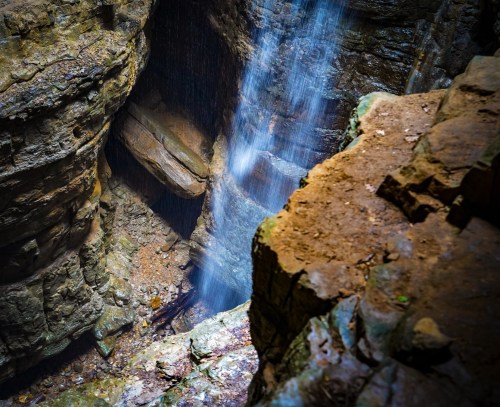 A waterfall cascading down a rocky cliff into a deep canyon, surrounded by rugged stone walls.