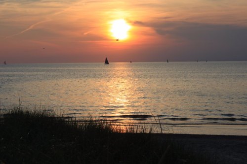 A serene sunset over a calm sea, with sailboats silhouetted against the colorful sky and gentle waves lapping at the shore.