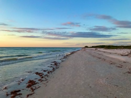 A serene beach at sunset, with gentle waves, sandy shore, and a clear sky dotted with clouds.
