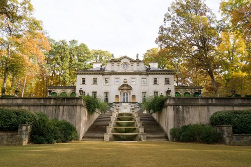 A grand, historic mansion surrounded by colorful autumn trees and a staircase leading to the entrance.