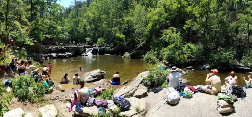 A sunny day at a natural swimming area with people relaxing by the water and enjoying the outdoors.