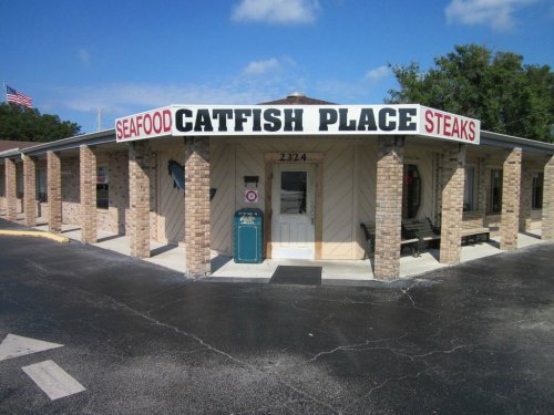 A restaurant building with a sign reading "Seafood Catfish Place Steaks," featuring a brick exterior and blue sky.