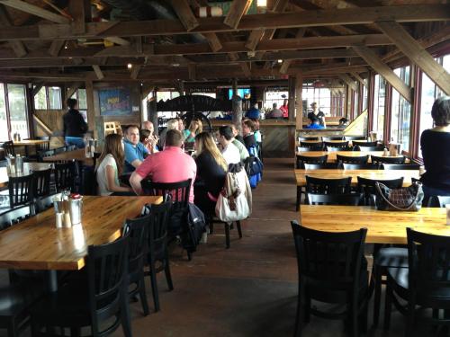 A rustic restaurant interior with wooden tables and chairs, featuring a group of people seated at a long table.