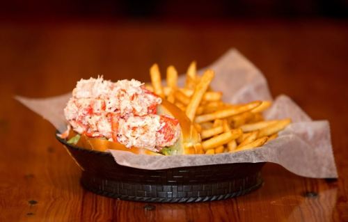 A lobster roll topped with fresh lobster meat, served with a side of crispy French fries in a basket.