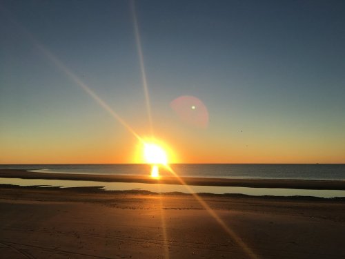 A serene beach at sunset, with vibrant orange and yellow hues reflecting on the water and a clear sky.