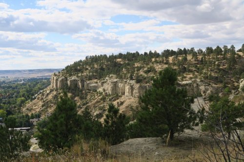A scenic view of a rocky hillside with trees under a partly cloudy sky.