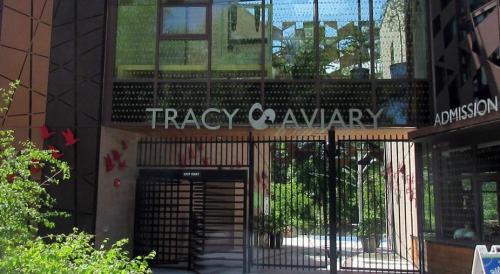 Entrance to Tracy Aviary, featuring a modern design with glass and metal, surrounded by greenery and decorative birds.