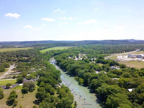 Aerial view of a lush green landscape with a winding river, dotted with boats, and a clear blue sky above.