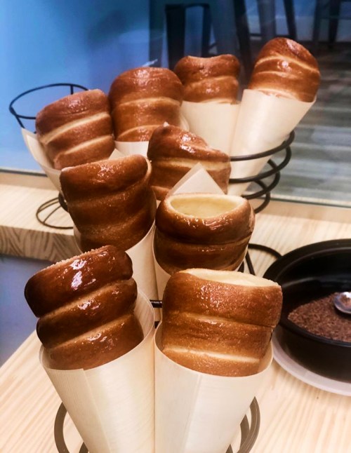 A display of freshly baked, golden-brown pastries in cone-shaped holders, drizzled with syrup.