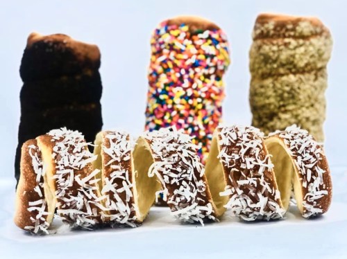 A variety of colorful donuts, including ones with sprinkles and coconut, arranged in a row against a light background.