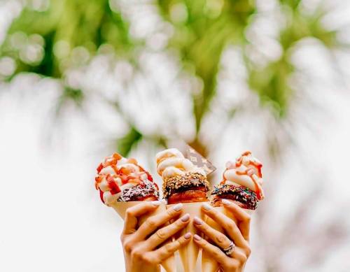 Three ice cream cones with various toppings held up against a blurred green background.