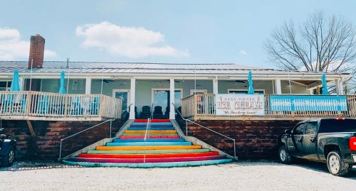 Colorful steps lead to a charming ice cream shop with a porch and blue accents under a clear sky.