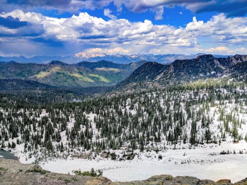 A panoramic view of a snow-covered valley surrounded by mountains under a partly cloudy sky.