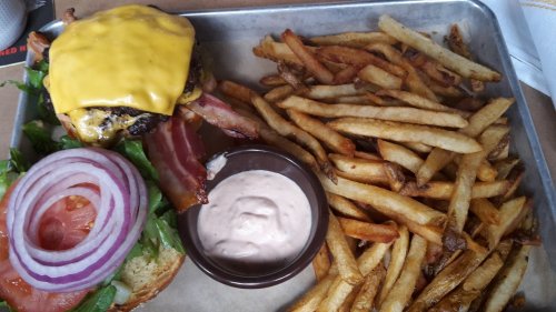 A cheeseburger with bacon, lettuce, tomato, and onion, served with a side of crispy fries and dipping sauce.