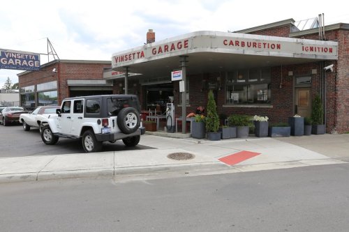 A vintage garage with a sign reading "Vinsetta Garage," featuring a parked Jeep and potted plants outside.