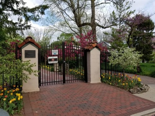 A wrought iron gate surrounded by blooming trees and colorful tulips, leading into a garden area.