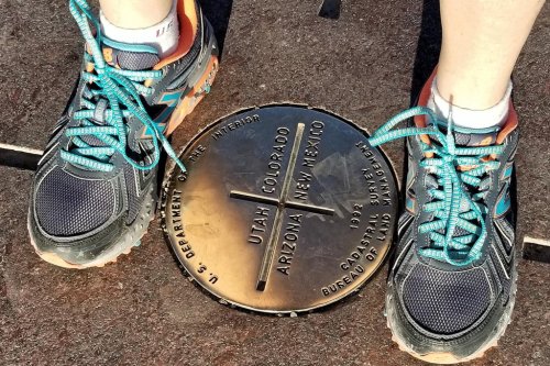 Person's feet in sneakers standing on a bronze marker indicating the Four Corners of Utah, Colorado, Arizona, and New Mexico.