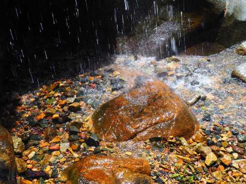 Water cascades over colorful stones, creating a serene scene with glistening droplets and a rocky surface.