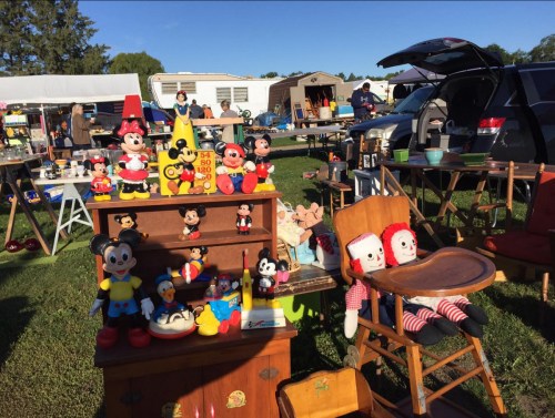 A vibrant flea market scene featuring various vintage Mickey and Minnie Mouse toys, dolls, and furniture on display.