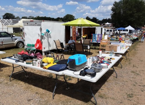 A bustling outdoor market scene with tables filled with various items for sale, including household goods and furniture.