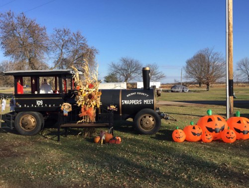 A vintage train display with pumpkins and autumn decorations at a swap meet, set against a clear blue sky.