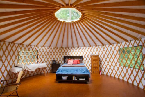 Cozy yurt interior featuring a bed, wooden furniture, and large windows with a circular skylight above.
