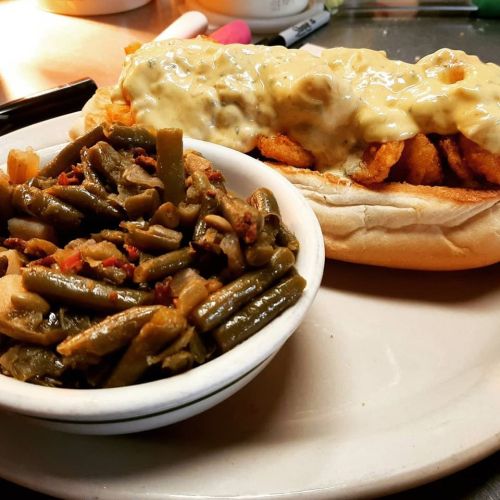 A plate featuring a sandwich with shrimp and cheese sauce, alongside a bowl of seasoned green beans.