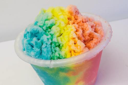 A colorful cup of rainbow shaved ice with vibrant layers of blue, green, yellow, orange, and pink.