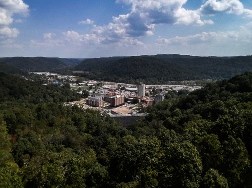 Aerial view of a valley with buildings and greenery, under a blue sky with scattered clouds.