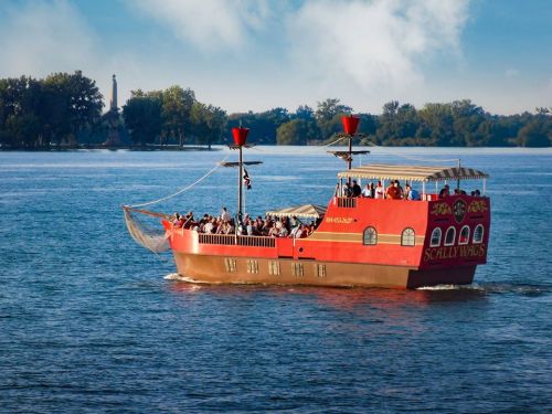 A colorful pirate-themed boat with passengers sailing on a calm river under a blue sky.