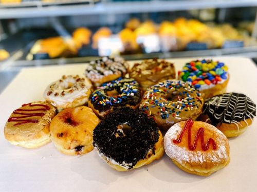 A variety of colorful donuts with different toppings arranged on a white surface, showcasing sprinkles, chocolate, and icing.