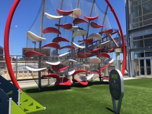Colorful climbing structure with red and white elements against a blue sky, set on green grass in an outdoor space.
