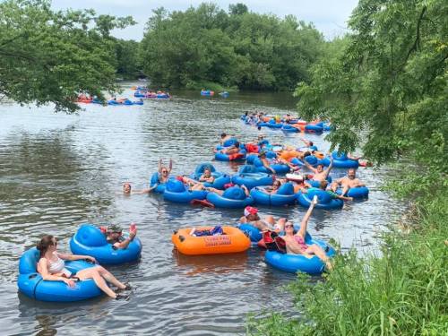 A group of people floating on blue inner tubes in a river, surrounded by trees and enjoying a sunny day.