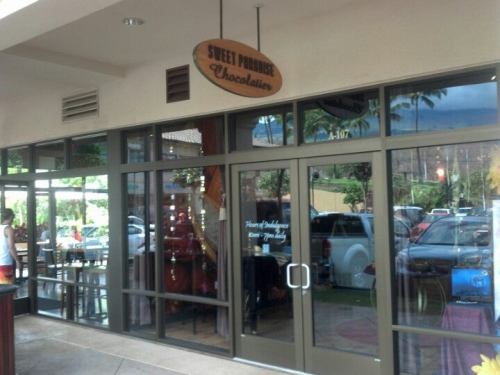 Exterior view of "Sweet Promises Chocolatier" shop with large glass windows and a sign above the entrance.