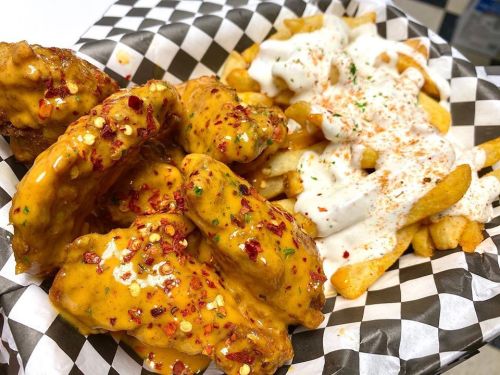 A plate of spicy chicken wings topped with red pepper flakes, served with seasoned fries and a creamy dipping sauce.